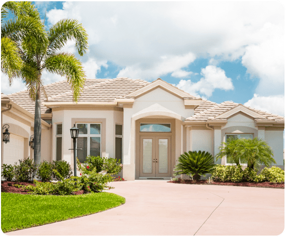 A modern, single-story house with a tiled roof, palm trees, and a curved driveway under a partly cloudy sky.
